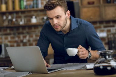 Man drinking coffee and using laptop clipart