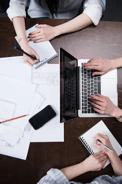 Femmes d'affaires écrivant dans des carnets et travaillant sur un ordinateur portable — Photo de stock