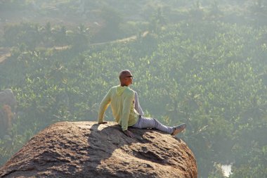 Gözlük yakışıklı bir kel adam Hampi, bir gün batımı veya şafak arka planda dağın tepesinde oturuyor. Aşırı cesur bir adamdır. Hindistan, Vijayanagar, İstanbul, unesco.