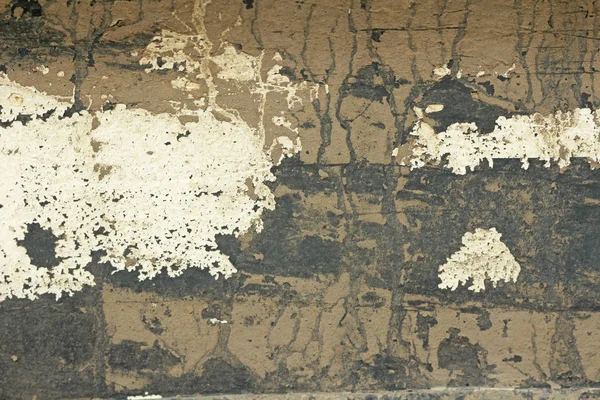 Old Flaky Paint Peeling off a Grungy Cracked Wall. Cracks Old Paint and Plaster on Background of Old Cement Wall. White, Gray and Beige Spots of Paint. An Old Cement Stone Wall as Vintage Cracked.