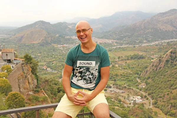 Bald man smiling in nature, against the background of mountains. Man is a traveler. The island of Sicily, Italy.