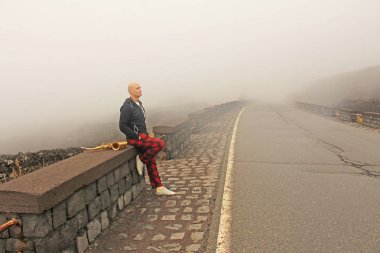 Kel bir adam bir altın alto saksafon yol kenarında sis ve yol arka planı üzerinde çalış. Romantik saksofon. Caz. Adam bir müzisyendir. Sicilya Adası, İtalya. Etna yanardağı.