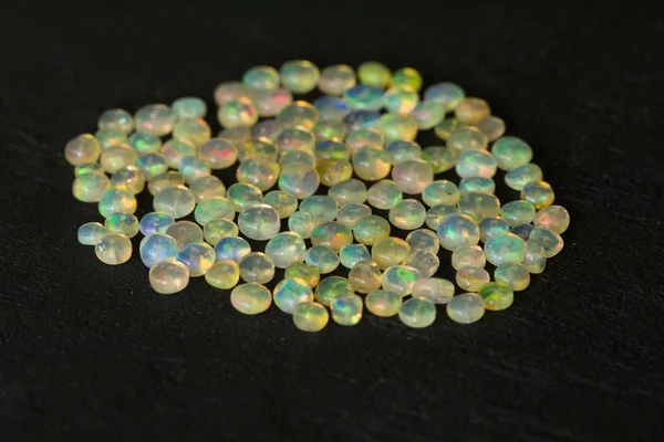 Opals ädelsten från Etiopien ligger på svart bakgrund. Vita eldopaler med regnbågsliknande eld. Naturlig eld Etiopisk opal, små stenar för att skapa smycken. Handgjorda smycken av sten. En stenhög. — Stockfoto