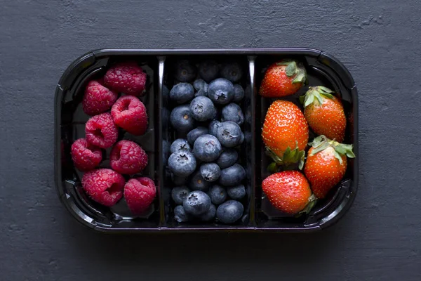 Fresh Sweet Berries strawberries, blueberries and raspberries lie in the tray, box on Black Background. Harvest Concept. Mix berries on a black background. Fruits with copy space for text