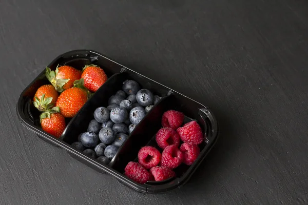 Fresh Sweet Berries strawberries, blueberries and raspberries lie in the tray, box on Black Background. Harvest Concept. Mix berries on a black background. Fruits with copy space for text