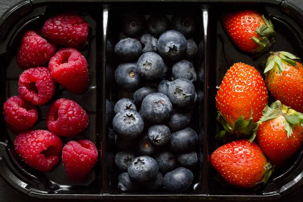 Fresh Sweet Berries strawberries, blueberries and raspberries lie in the tray, box on Black Background. Harvest Concept. Mix berries on a black background. Fruits with copy space for text