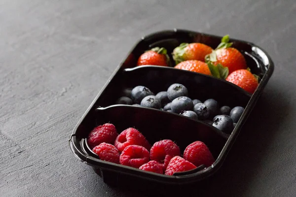 Fresh Sweet Berries strawberries, blueberries and raspberries lie in the tray, box on Black Background. Harvest Concept. Mix berries on a black background. Fruits with copy space for text