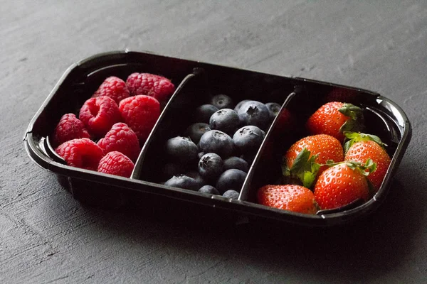 Fresh Sweet Berries strawberries, blueberries and raspberries lie in the tray, box on Black Background. Harvest Concept. Mix berries on a black background. Fruits with copy space for text