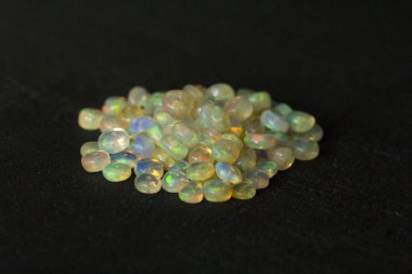 Etiyopya 'dan Opals mücevheri siyah arka planda yatıyor. Gökkuşağı gibi ateşi olan beyaz ateş opalleri. Doğal ateş Etiyopya opalı, mücevher yapmak için küçük taşlar. El yapımı taş mücevherler. Taş yığını.