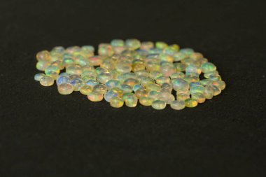 Etiyopya 'dan Opals mücevheri siyah arka planda yatıyor. Gökkuşağı gibi ateşi olan beyaz ateş opalleri. Doğal ateş Etiyopya opalı, mücevher yapmak için küçük taşlar. El yapımı taş mücevherler. Taş yığını.