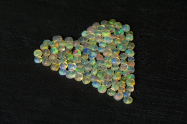 Etiyopya 'dan Opals mücevheri siyah arka planda yatıyor. Gökkuşağı gibi ateşi olan beyaz ateş opalleri. Doğal ateş Etiyopya opalı, mücevher yapmak için küçük taşlar. El yapımı taş mücevherler. Aşk, Kalp Taşları