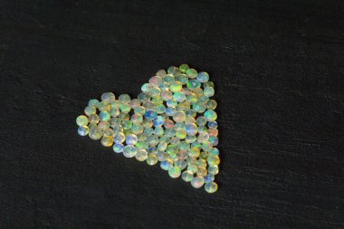 Etiyopya 'dan Opals mücevheri siyah arka planda yatıyor. Gökkuşağı gibi ateşi olan beyaz ateş opalleri. Doğal ateş Etiyopya opalı, mücevher yapmak için küçük taşlar. El yapımı taş mücevherler. Aşk, Kalp Taşları