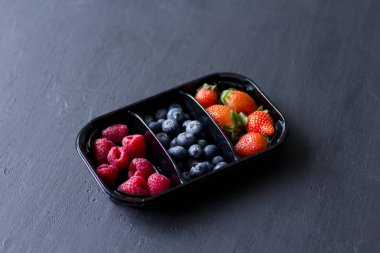 Taze tatlı çilekler, yabanmersinleri ve ahududular tepside duruyor, kutuda Kara Arkaplan 'da. Hasat Konsepti. Siyah arka planda böğürtlenleri karıştır. Metin için kopyalama alanı olan meyveler