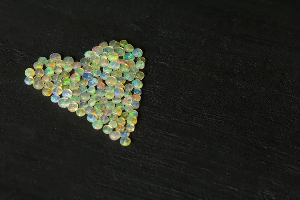 Ópalos de piedra preciosa de Etiopía se encuentra en el fondo negro. Ópalos de fuego blanco con fuego como arco iris. Fuego natural ópalo etíope, piedras pequeñas para crear joyas. Joyería artesanal de piedra. Amor, Piedras del corazón — Foto de Stock