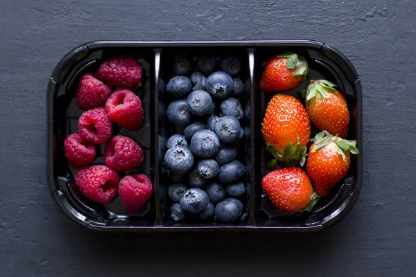 Fresh Sweet Berries strawberries, blueberries and raspberries lie in the tray, box on Black Background. Harvest Concept. Mix berries on a black background. Fruits with copy space for text