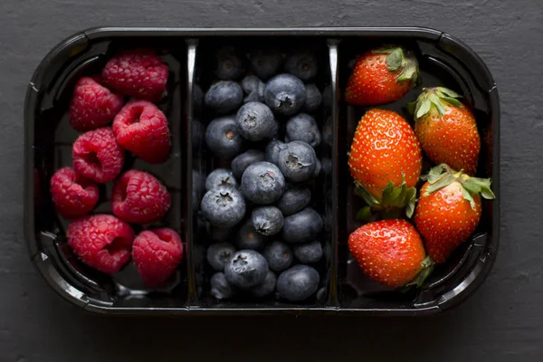 新鮮な甘いベリーイチゴ、ブルーベリー、ラズベリーがトレイにあり、ブラックバックグランドの箱に入っています。収穫の概念。黒の背景に果実を混ぜます。テキストのためのコピースペースを持つ果物 — ストック写真