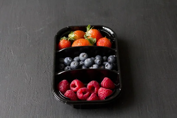 Fresh Sweet Berries strawberries, blueberries and raspberries lie in the tray, box on Black Background. Harvest Concept. Mix berries on a black background. Fruits with copy space for text