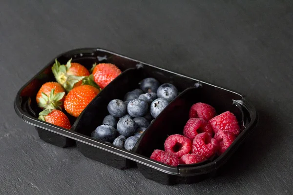 Fresh Sweet Berries strawberries, blueberries and raspberries lie in the tray, box on Black Background. Harvest Concept. Mix berries on a black background. Fruits with copy space for text