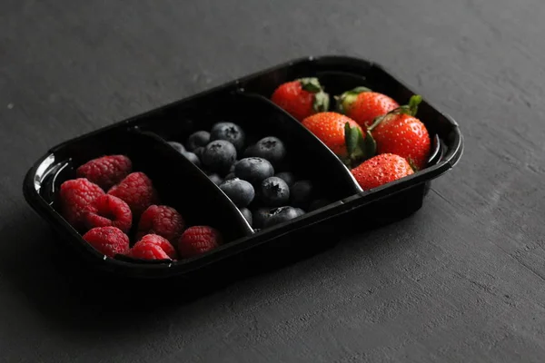 Fresh Sweet Berries strawberries, blueberries and raspberries lie in the tray, box on Black Background. Harvest Concept. Mix berries on a black background. Fruits with copy space for text
