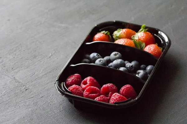 Fresh Sweet Berries strawberries, blueberries and raspberries lie in the tray, box on Black Background. Harvest Concept. Mix berries on a black background. Fruits with copy space for text