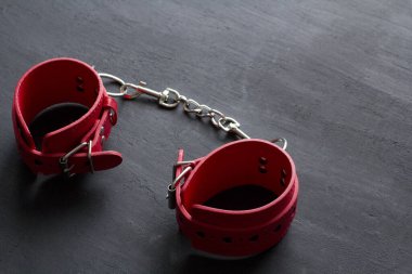 BDSM, kölelik oyunu, fetiş aşınma ve yakın plan seks oyuncağı konsepti, siyah arka planda kırmızı deri kelepçeler. Yetişkin oyunları ve oyuncaklar.
