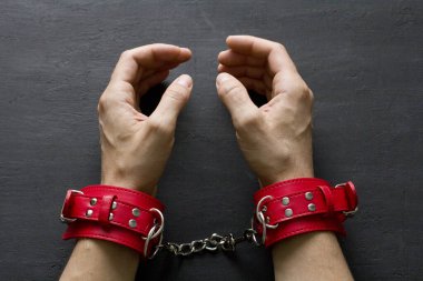 Yetişkin erkek elleri kırmızı erotik deri kelepçeli. Eller esaret altında. Siyah arka planda kırmızı deri kelepçeler. Yetişkin oyunları ve oyuncaklar. BDSM, fetiş aşınma ve yakın plan seks oyuncağı konsepti.