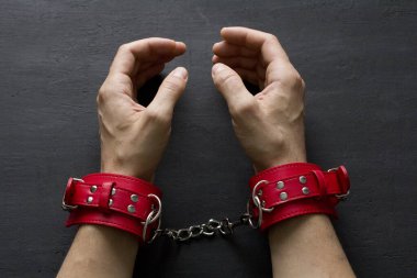 Yetişkin erkek elleri kırmızı erotik deri kelepçeli. Eller esaret altında. Siyah arka planda kırmızı deri kelepçeler. Yetişkin oyunları ve oyuncaklar. BDSM, fetiş aşınma ve yakın plan seks oyuncağı konsepti.