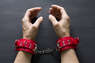 Yetişkin erkek elleri kırmızı erotik deri kelepçeli. Eller esaret altında. Siyah arka planda kırmızı deri kelepçeler. Yetişkin oyunları ve oyuncaklar. BDSM, fetiş aşınma ve yakın plan seks oyuncağı konsepti.