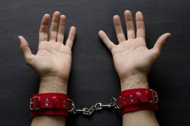 Yetişkin erkek elleri kırmızı erotik deri kelepçeli. Eller esaret altında. Siyah arka planda kırmızı deri kelepçeler. Yetişkin oyunları ve oyuncaklar. BDSM, fetiş aşınma ve yakın plan seks oyuncağı konsepti.