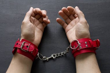 Yetişkin erkek elleri kırmızı erotik deri kelepçeli. Eller esaret altında. Siyah arka planda kırmızı deri kelepçeler. Yetişkin oyunları ve oyuncaklar. BDSM, fetiş aşınma ve yakın plan seks oyuncağı konsepti.