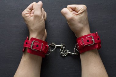 Yetişkin erkek elleri kırmızı erotik deri kelepçeli. Eller esaret altında. Siyah arka planda kırmızı deri kelepçeler. Yetişkin oyunları ve oyuncaklar. BDSM, fetiş aşınma ve yakın plan seks oyuncağı konsepti.