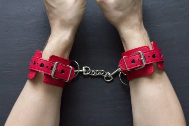 Yetişkin erkek elleri kırmızı erotik deri kelepçeli. Eller esaret altında. Siyah arka planda kırmızı deri kelepçeler. Yetişkin oyunları ve oyuncaklar. BDSM, fetiş aşınma ve yakın plan seks oyuncağı konsepti.