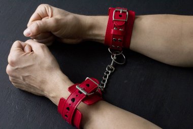 Yetişkin erkek elleri kırmızı erotik deri kelepçeli. Eller esaret altında. Siyah arka planda kırmızı deri kelepçeler. Yetişkin oyunları ve oyuncaklar. BDSM, fetiş aşınma ve yakın plan seks oyuncağı konsepti.