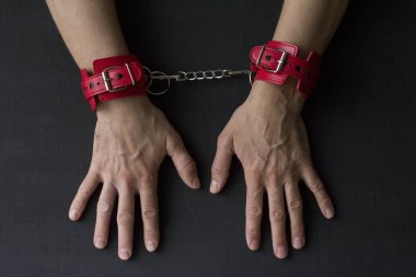 Yetişkin erkek elleri kırmızı erotik deri kelepçeli. Eller esaret altında. Siyah arka planda kırmızı deri kelepçeler. Yetişkin oyunları ve oyuncaklar. BDSM, fetiş aşınma ve yakın plan seks oyuncağı konsepti.