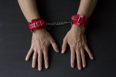 Yetişkin erkek elleri kırmızı erotik deri kelepçeli. Eller esaret altında. Siyah arka planda kırmızı deri kelepçeler. Yetişkin oyunları ve oyuncaklar. BDSM, fetiş aşınma ve yakın plan seks oyuncağı konsepti.
