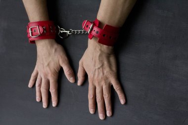 Yetişkin erkek elleri kırmızı erotik deri kelepçeli. Eller esaret altında. Siyah arka planda kırmızı deri kelepçeler. Yetişkin oyunları ve oyuncaklar. BDSM, fetiş aşınma ve yakın plan seks oyuncağı konsepti.