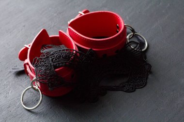 Kırmızı deri kelepçeler, siyah arka planda erotik siyah maske. Yetişkin oyunları ve oyuncaklar. BDSM, kölelik oyunu, fetiş aşınma ve yakın plan seks oyuncağı konsepti.