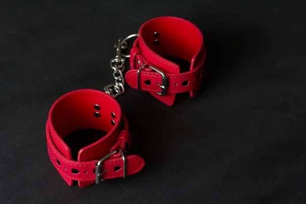 Red leather handcuffs on black background. Adult games and toys. BDSM, bondage play, fetish wear and kinky sex toy concept with close up.