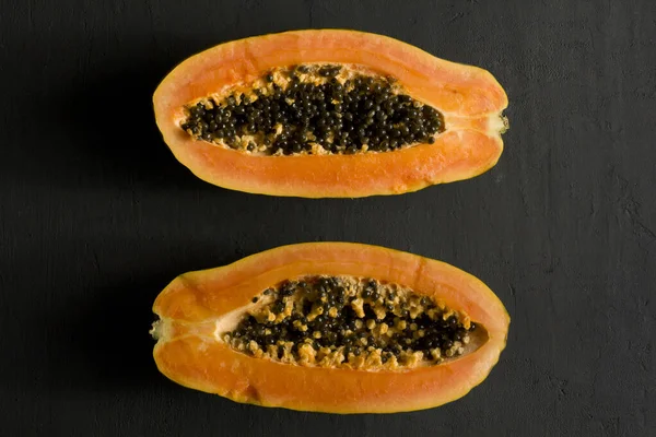 Two halves of papaya fruit cut in half, lie on black modern background. Black seeds of sweet, orange papaya. Vegetarianism, healthy nutrition, diet. Tropical fruits.Top view. Copy space. Flat lay.
