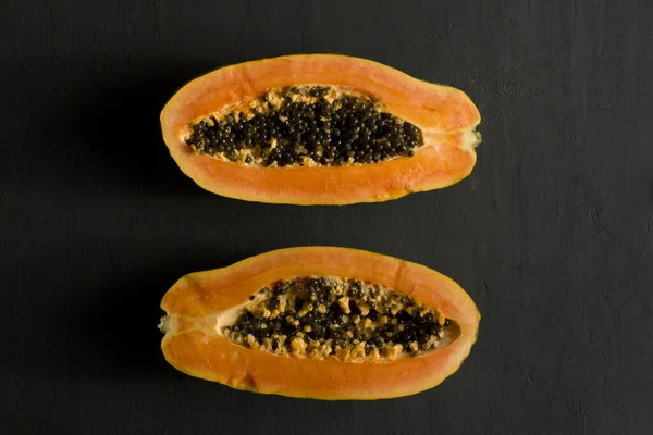 Two halves of papaya fruit cut in half, lie on black modern background. Black seeds of sweet, orange papaya. Vegetarianism, healthy nutrition, diet. Tropical fruits.Top view. Copy space. Flat lay.