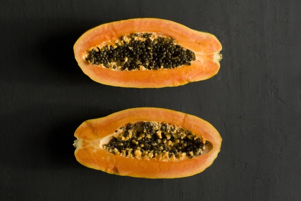 Two halves of papaya fruit cut in half, lie on black modern background. Black seeds of sweet, orange papaya. Vegetarianism, healthy nutrition, diet. Tropical fruits.Top view. Copy space. Flat lay.