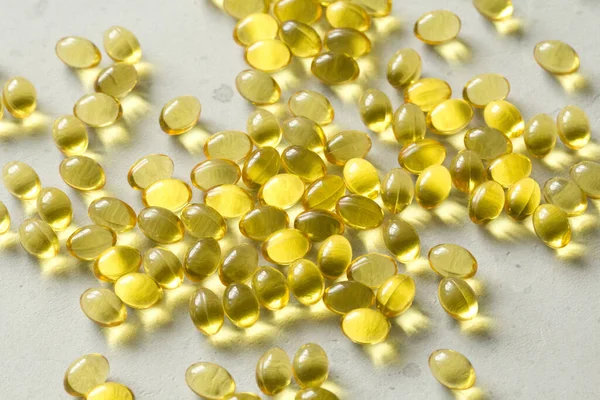 Pile of transparent capsules of golden yellow color lies on light gray modern background. Oil filled capsules vitamin A, vitamin D3, fish oil, omega 3, 6, 9, evening primrose, vitamin D, vitamin E.