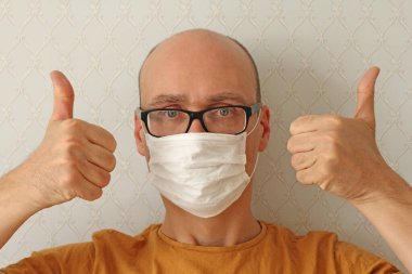 Tıbbi maskeli genç adam. Enfeksiyonu önlemek için hijyenik maske takan adam, grip gibi hava yoluyla bulaşan solunum hastalığı, Covid - 2019. Coronavirus. Bir erkek elleriyle beğenilerini gösterir, başparmaklarıyla..
