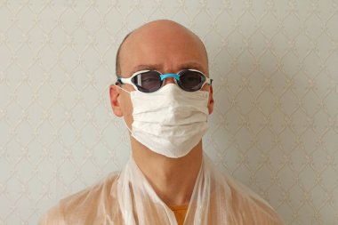 Tıbbi maskeli, gözlüklü, koruyucu elbiseli genç adam. Enfeksiyonu önlemek için hijyenik maske takan adam, grip gibi hava yoluyla bulaşan solunum hastalığı, Covid - 2019. Koronavirüs ve virüslere karşı koruma.