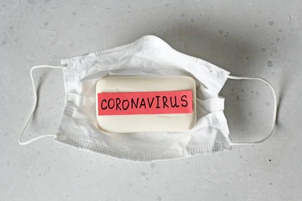 Protective medical hygiene mask, soap lie on light background, word coronavirus is written on soap. Hand washing, hygiene, for prevention of coronavirus, other viruses, to stop spread coronavirus.