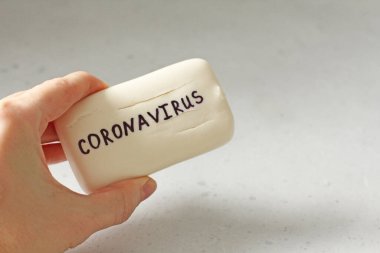 Coronavirus kelimesinin yazıldığı sabun kalıbını tutan el. Beyaz sabun kadının elinde yatıyor. Hijyen, koronavirüsün önlenmesi için virüsler, Coronavirus covid 2019 yayılmasını engellemek için. El yıkama..