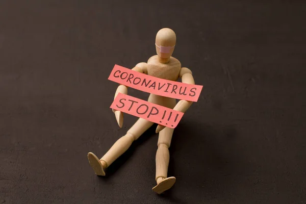Figure of wooden man sits and asks coronavirus to stop. Pandemic, panic, recovery, red words on a black background. Infections that are transmitted by airborne droplets. Wooden little men and people.