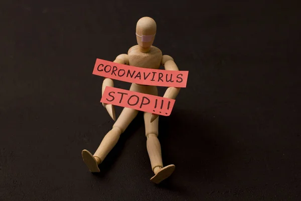 Figure of wooden man sits and asks coronavirus to stop. Pandemic, panic, recovery, red words on a black background. Infections that are transmitted by airborne droplets. Wooden little men and people.