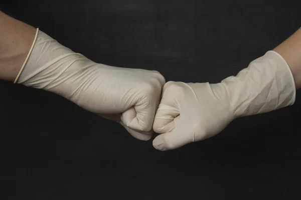 Greeting fist to fist in medical rubber gloves. Hands in white medical latex rubber gloves on black background. Protective disposable gloves protect against viruses, coronavirus, dangerous bacteria.