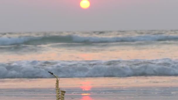 金色のサックスアルトは 海と太陽の背景を背景に 砂と海岸に立っています ロマンチックな音楽的背景 音楽のカバーと休日 コピースペース付きデザイン — ストック動画